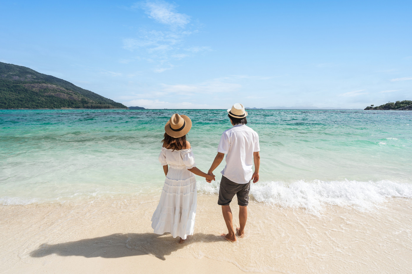 Young couple traveler relaxing and enjoying at beautiful tropical white sand beach with wave foam and transparent sea, Summer vacation and Travel concept