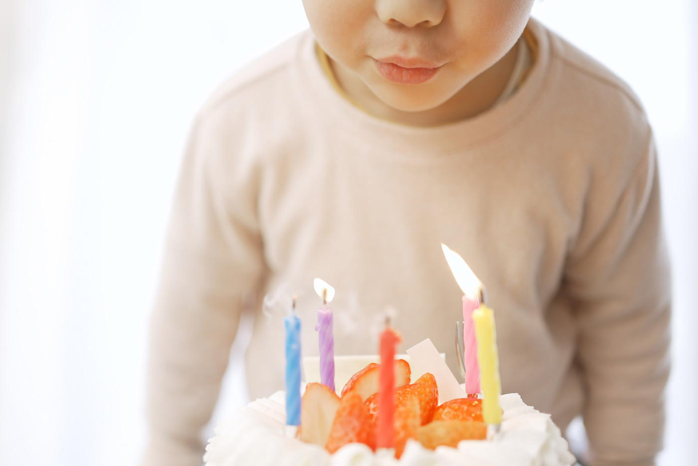 誕生日ケーキのロウソクの火を吹き消すアジア人の男の子