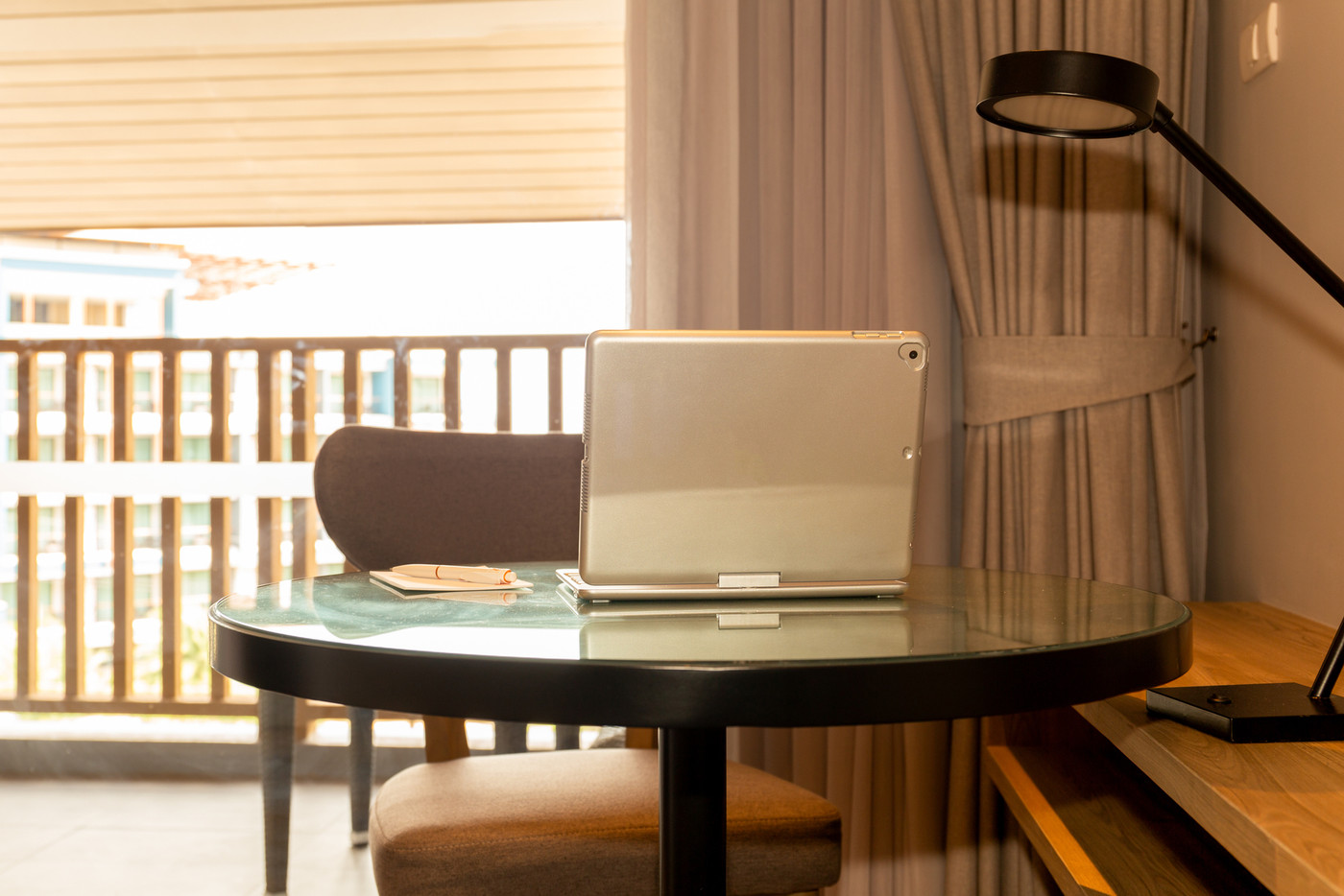 Laptop with pen and paper on table in hotel room.