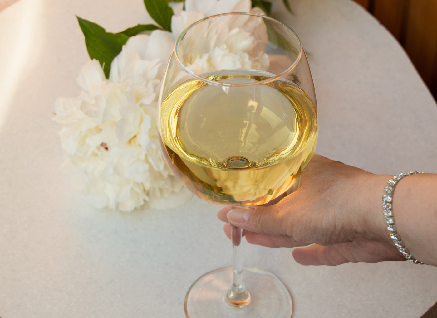 A glass of white wine holding woman's hand in the bracelet. Closeup