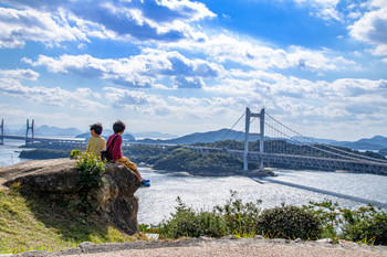 Brothers sitting together and looking at the Great Seto Bridge and the Seto Inland Sea, Kurashiki City Okayama Prefecture