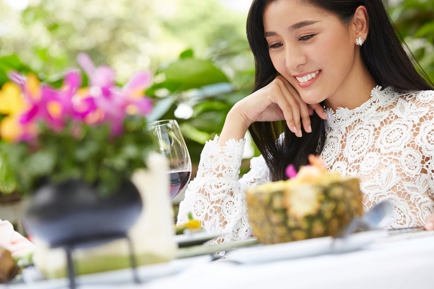 a gorgeous lady is smiling and looking at wine glass on a table in a restaurant