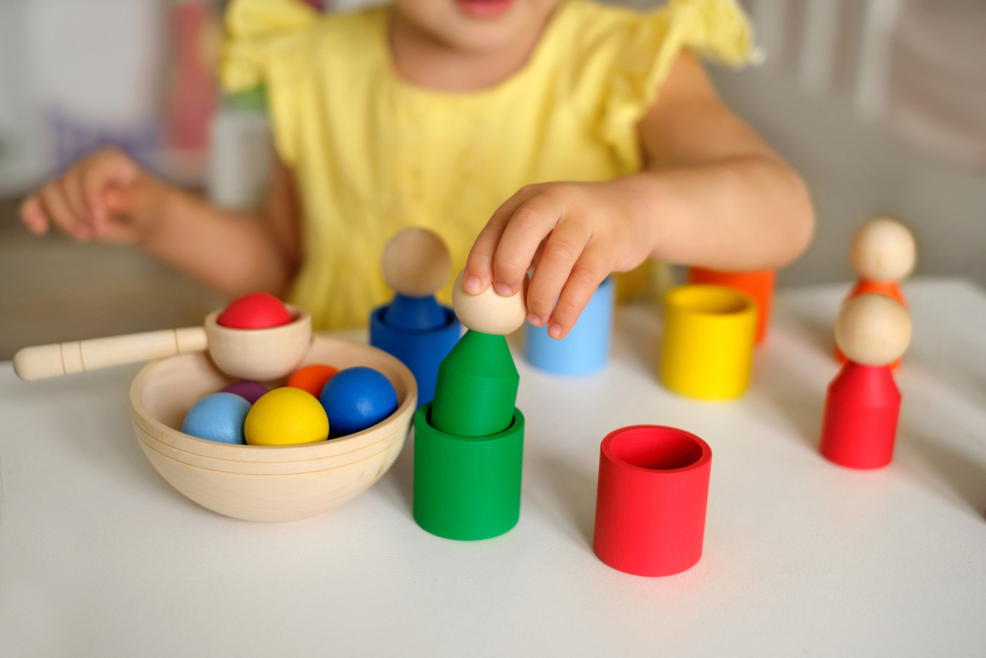 A sorter toy. Children's educational games.The child learns colors by playing with toy multi-colored wooden cylinders in the shape of a man and inserting them into cups of the appropriate co