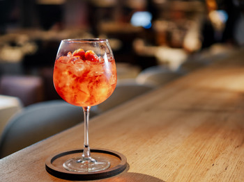 Transparent pink alcohol cocktail in wine glass with ice, aperol and gin on bar counter in restaurant interior. Alcohol drink Aperol Spritz aperitif cocktail. Cold alcoholic cocktail in bar