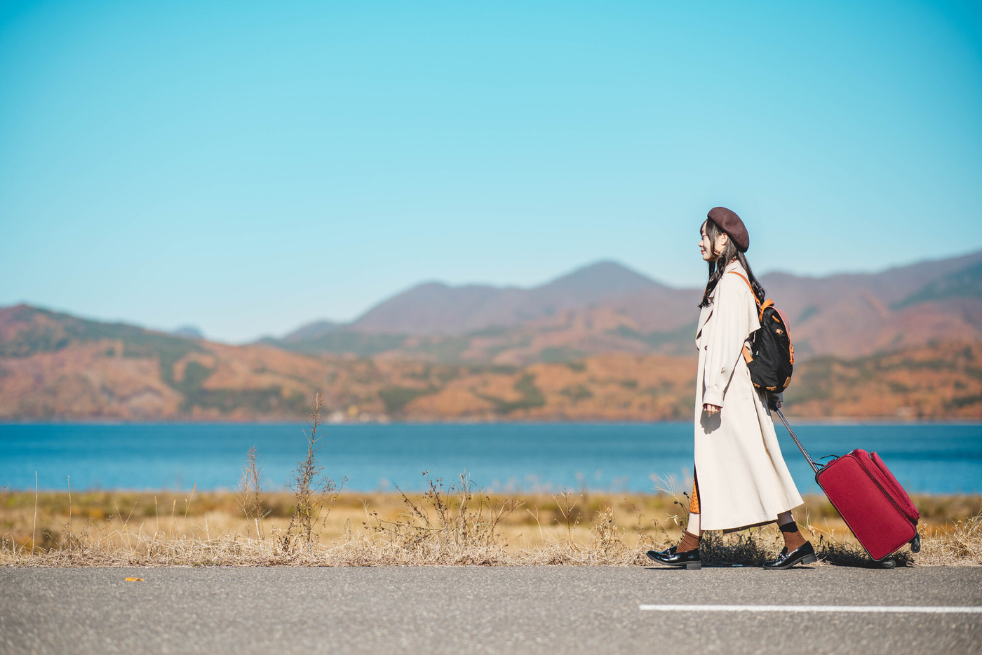 女子旅　キャリーバックを持って青空のもと歩いている若い女性