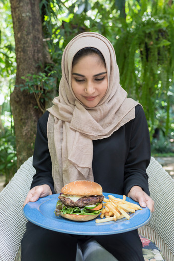 Happy Arabian woman holding a plate of burgers.