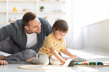 Cute little boy playing wooden train and railway with loving daddy, sitting together on floor at home, empty space