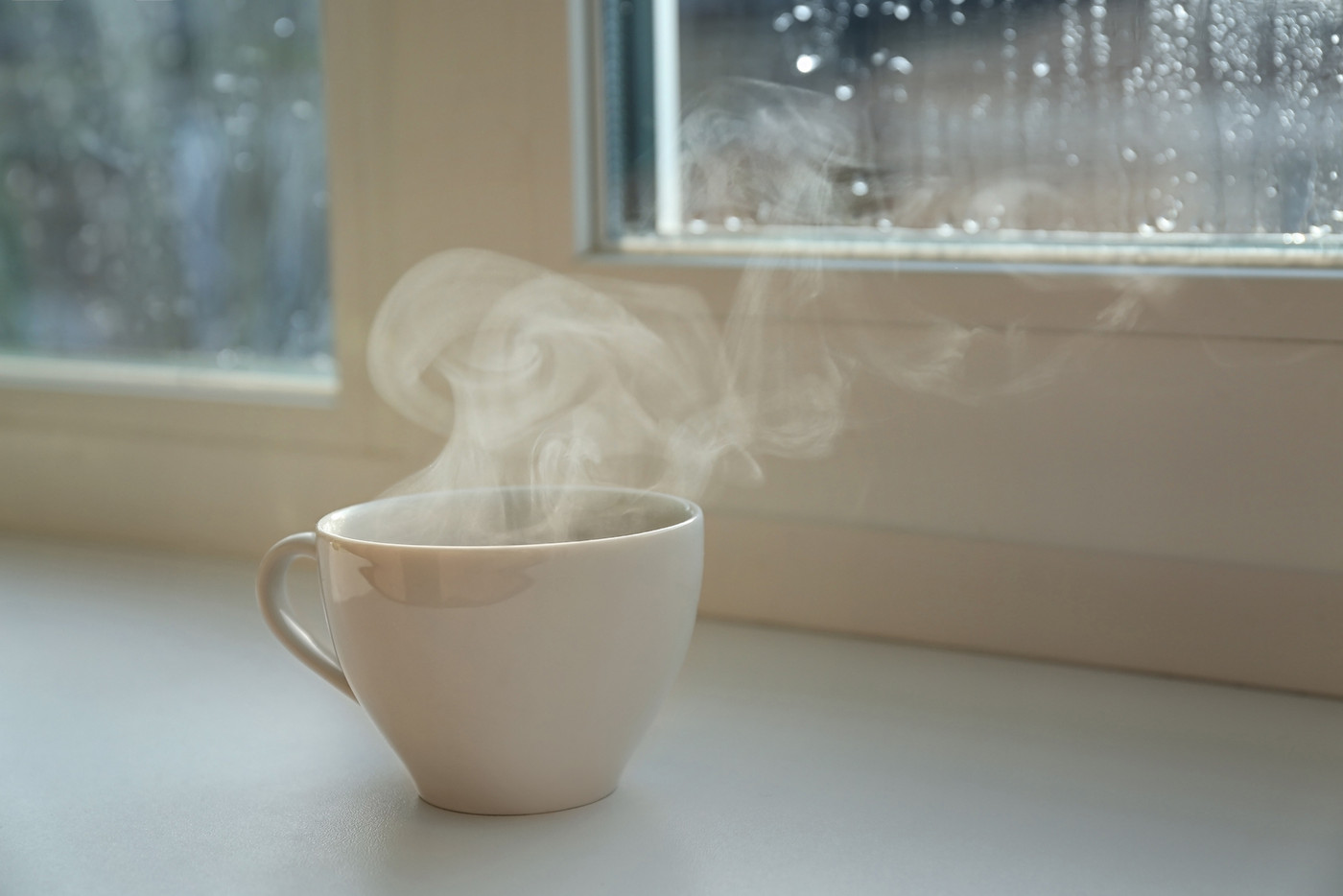 Cup of hot drink near window on rainy day. Space for text