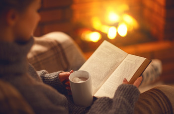 book and cup of coffee in hands of girl on winter evening near