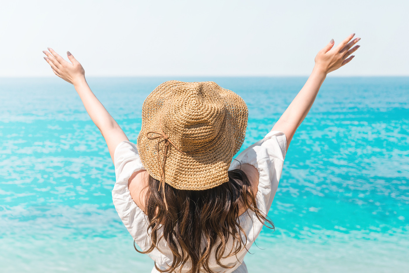 海に向かってバンザイする若い女性の後ろ姿(バカンス・夏・リゾート・南国・オーシャンビュー・海外旅行)