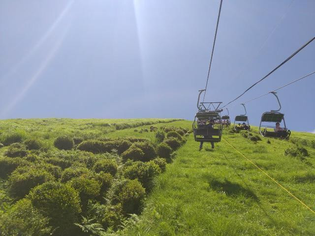「大室山」の山頂へ向かう、登山リフト。草の絨毯のような景色に癒されつつ、片道約6分の空中散歩を楽しめる / 1