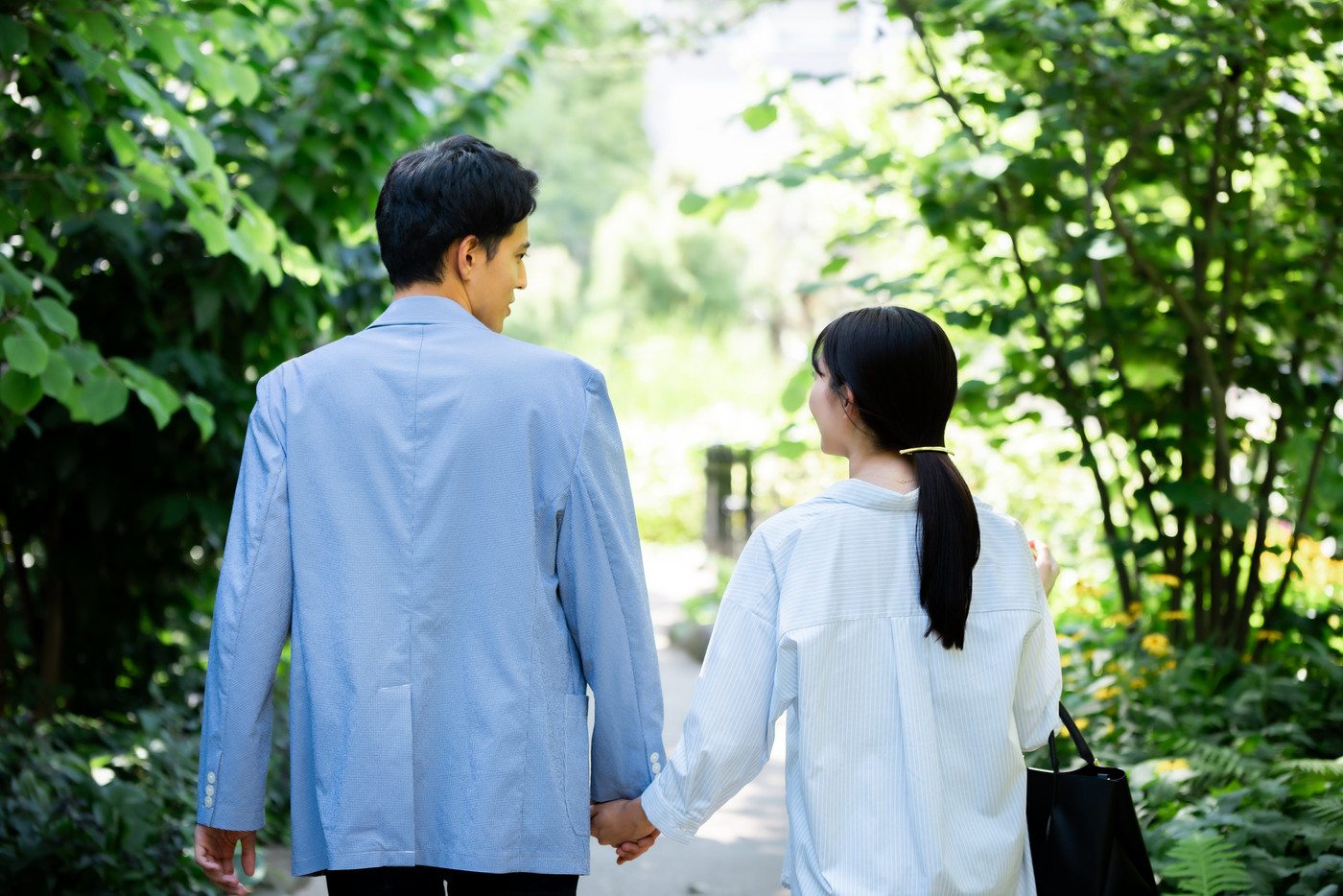 新緑の公園を歩くカップルの後ろ姿