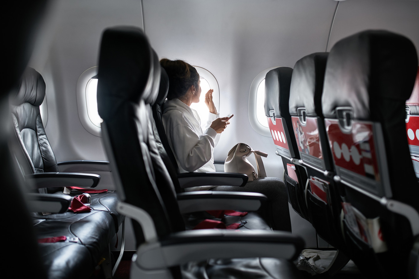 Woman with smartphone sits on black seat in plane