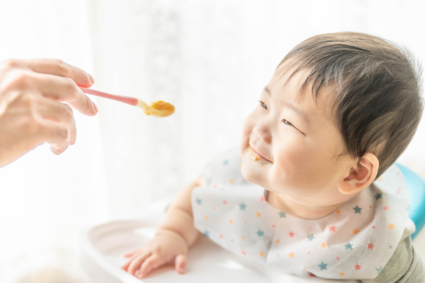 窓辺でベビーチェアに座って離乳食を食べる赤ちゃん