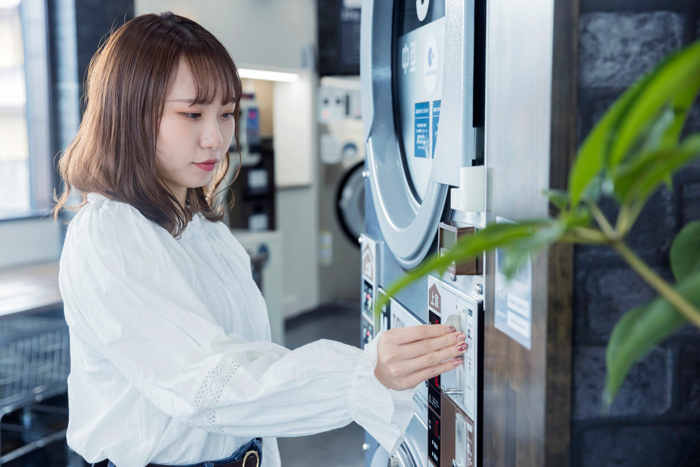 コインランドリーで洗濯をする若い女性 お金を入れる