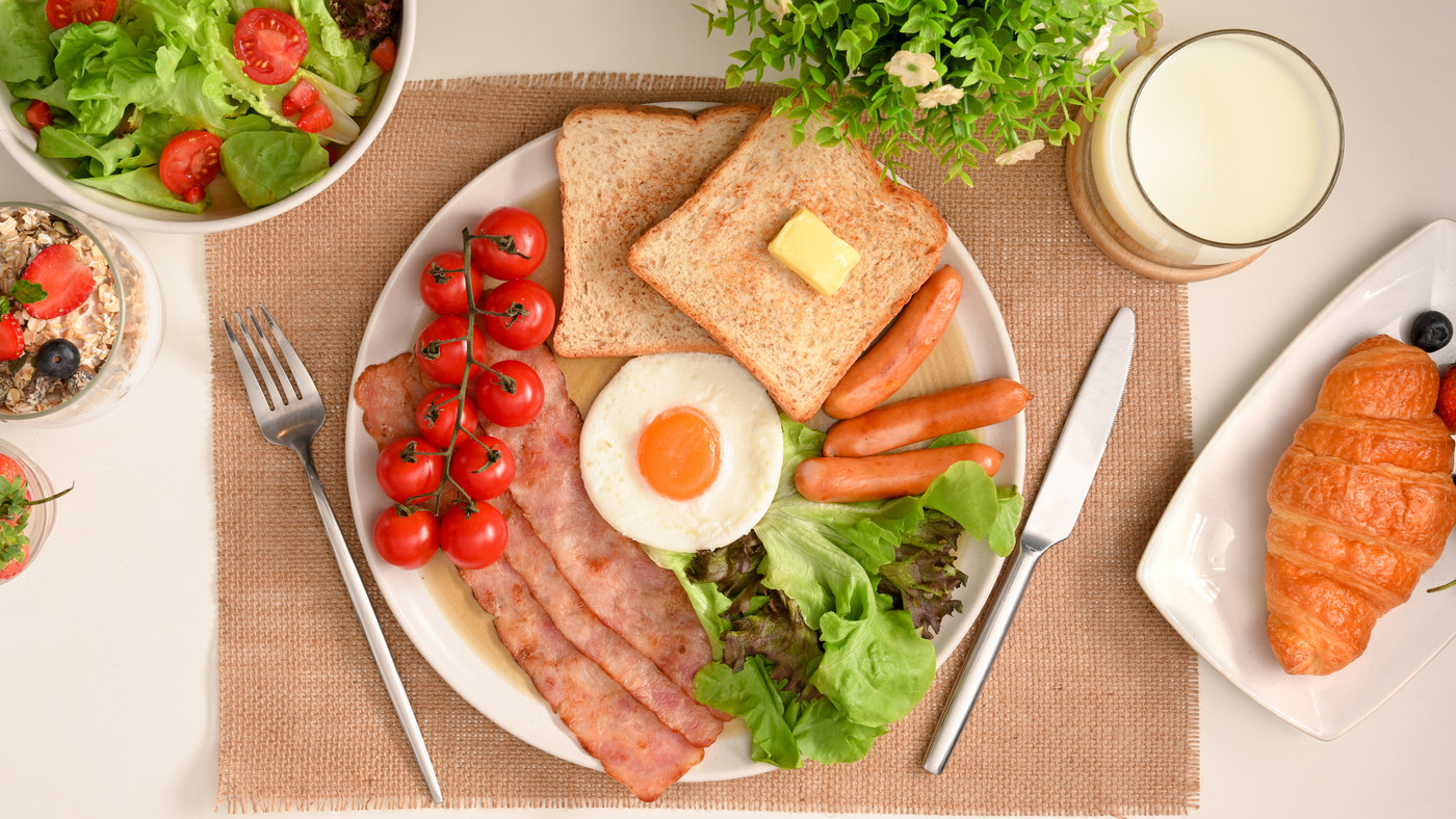 English breakfast set with egg, hams, sausages, toasts on table.