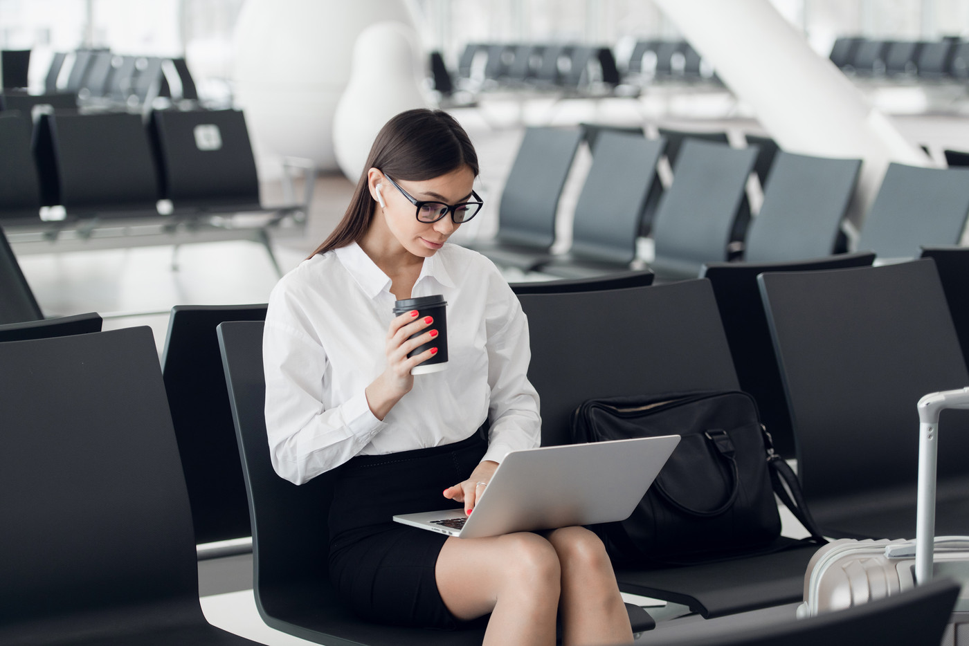 Young woman with coffee working on laptop sitting in a departure lounge of airport