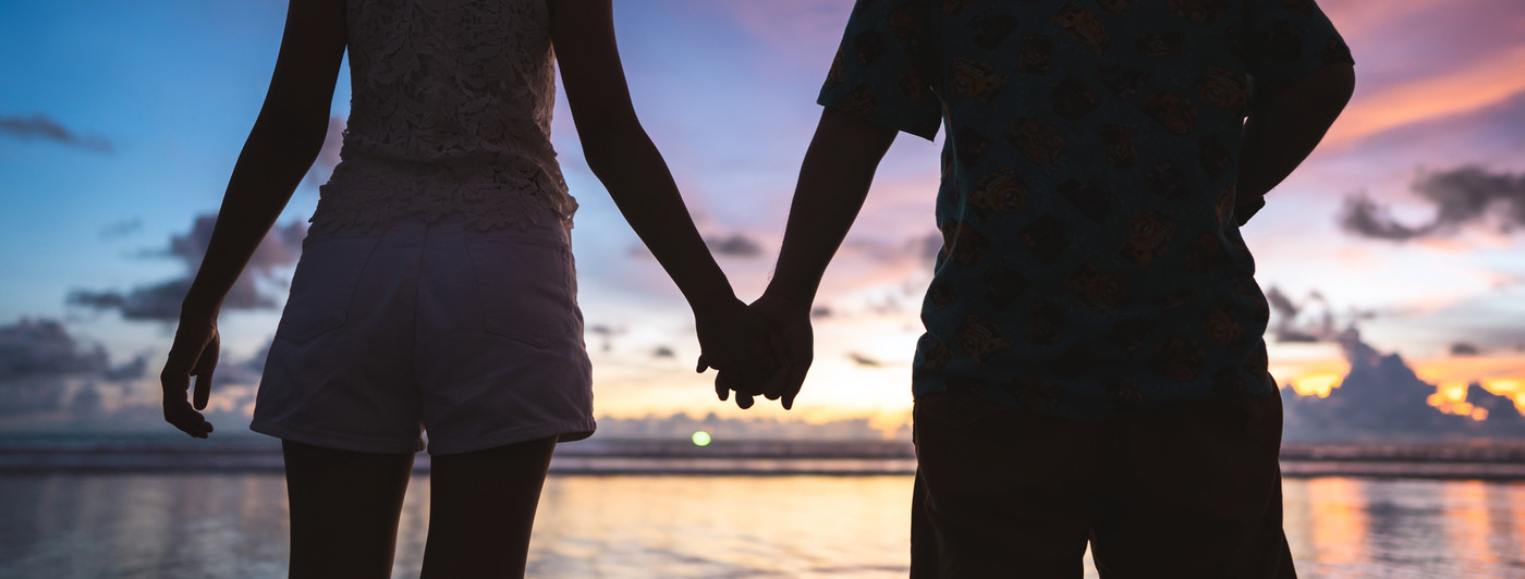 Rear view of adult tourist asian love couple holding hand on the beach with sunset sky background