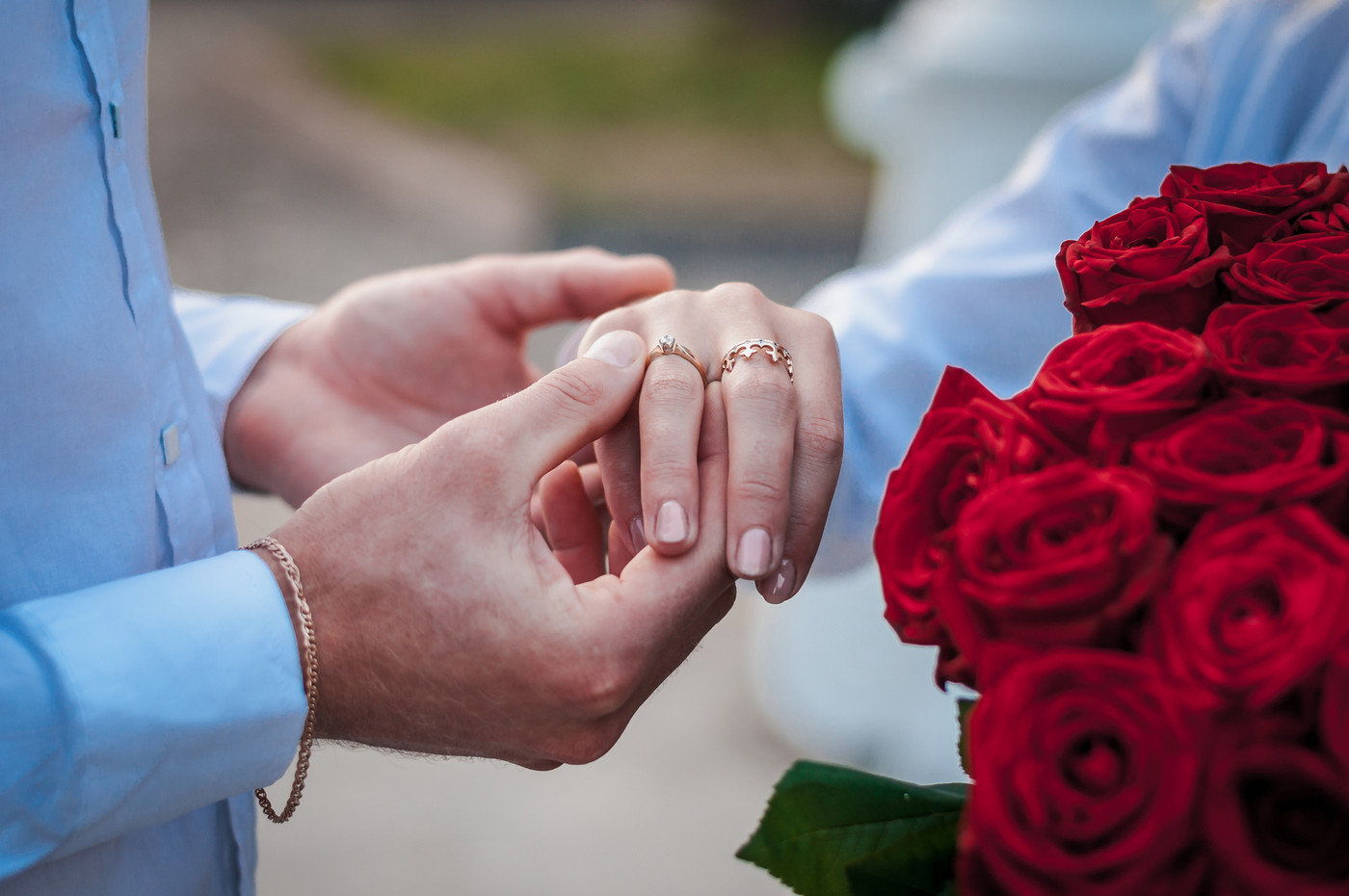 hands of newlyweds with wedding rings and bouquet with red roses