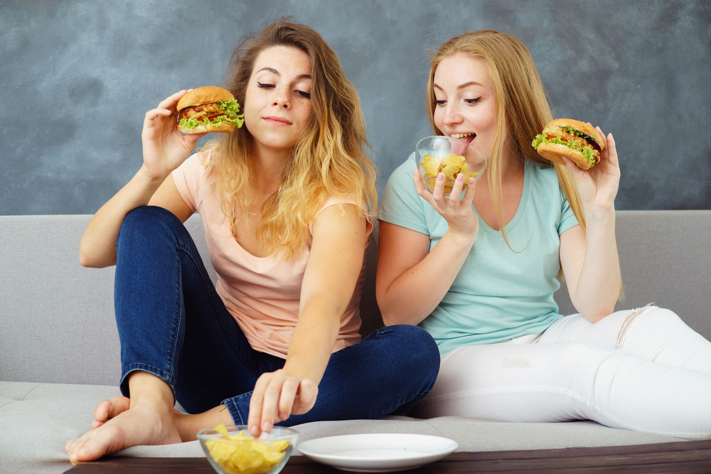 Two young women greedily eating burgers and chips