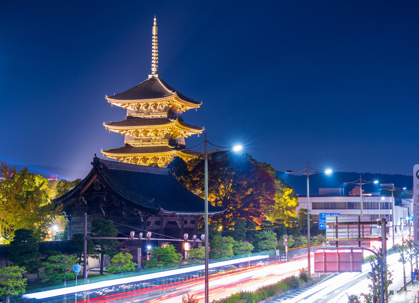 夜空にライトアップされ黄金色に輝く東のお寺の五重塔と走る車の光跡｜京都府京都市