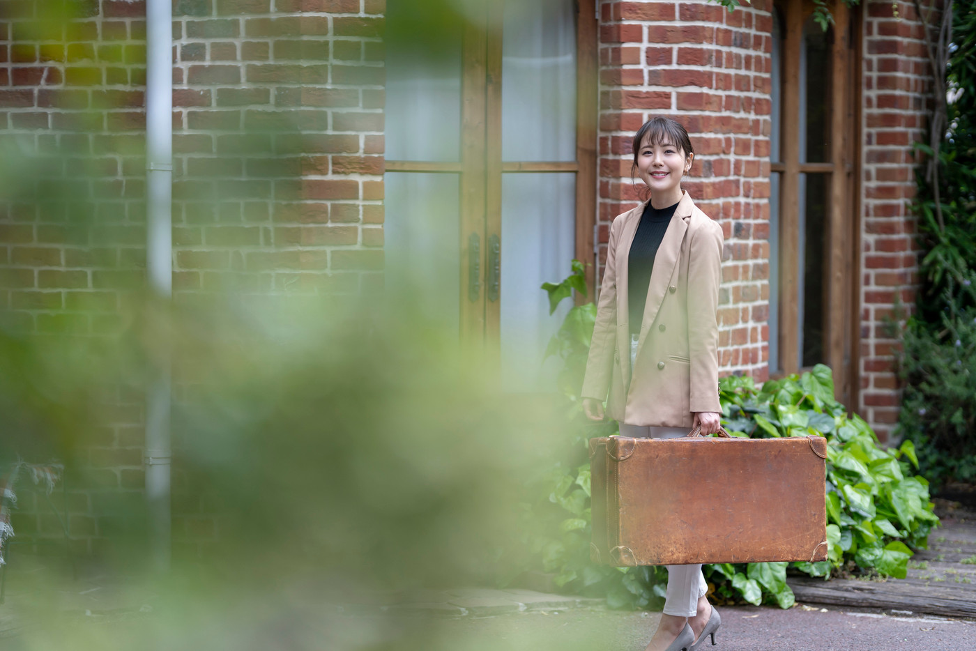 おしゃれなデザインのアンティークトランクケースと煉瓦造りの多い街並みを一人で観光する美人女性