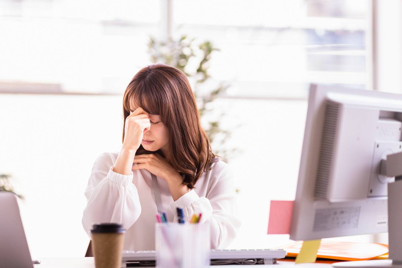 体調が優れないデスクワーク中の女性