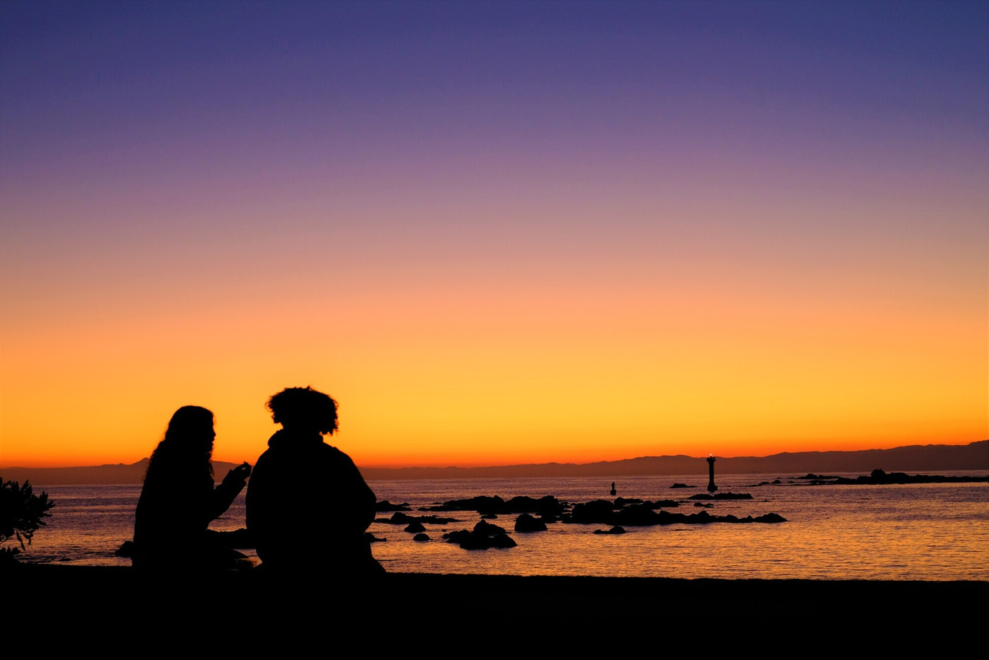 海辺で夕日を楽しむ外国人カップル