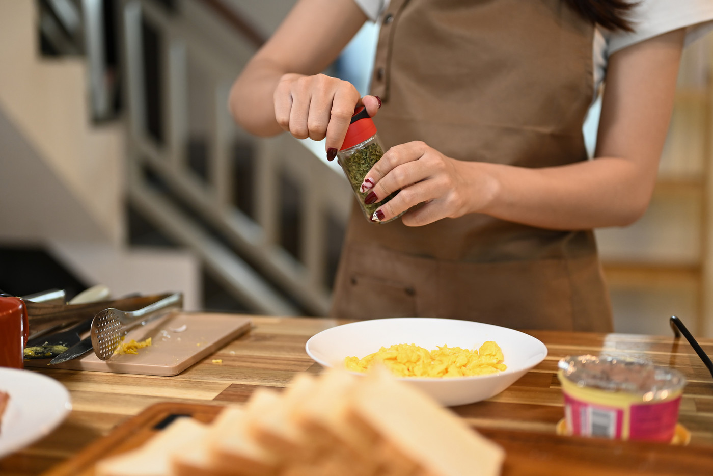 Woman add seasoning to a plate of scrambled eggs on a countertop