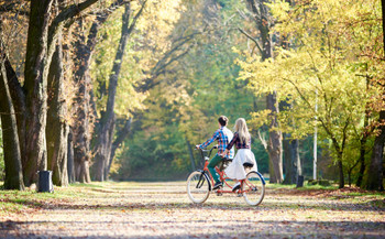 Young couple, handsome man and attractive woman on tandem bike in sunny summer park or forest.